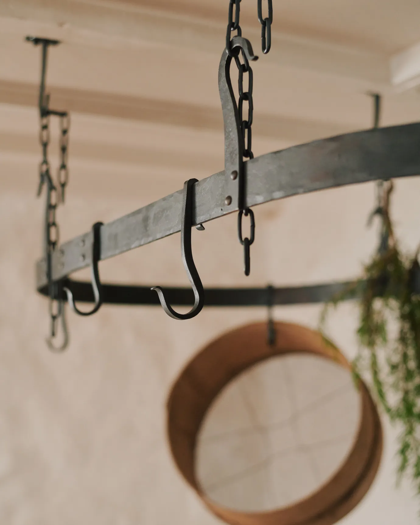 A close-up view of a large oval-shaped wrought iron pot hanger with several looped hooks which hang from the frame.